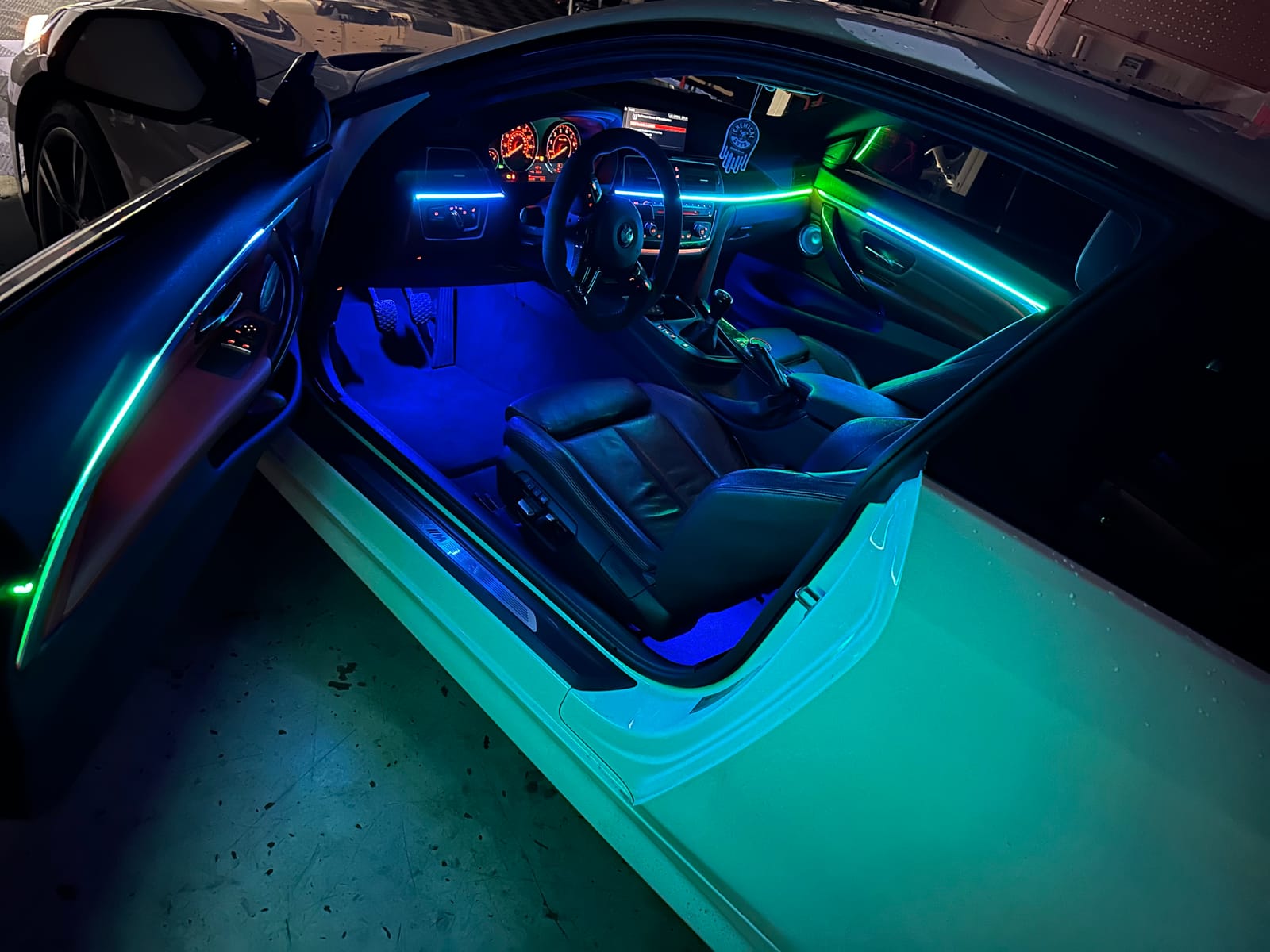 Teal and green ambient lighting along the doors and dash of a white BMW with the door open
