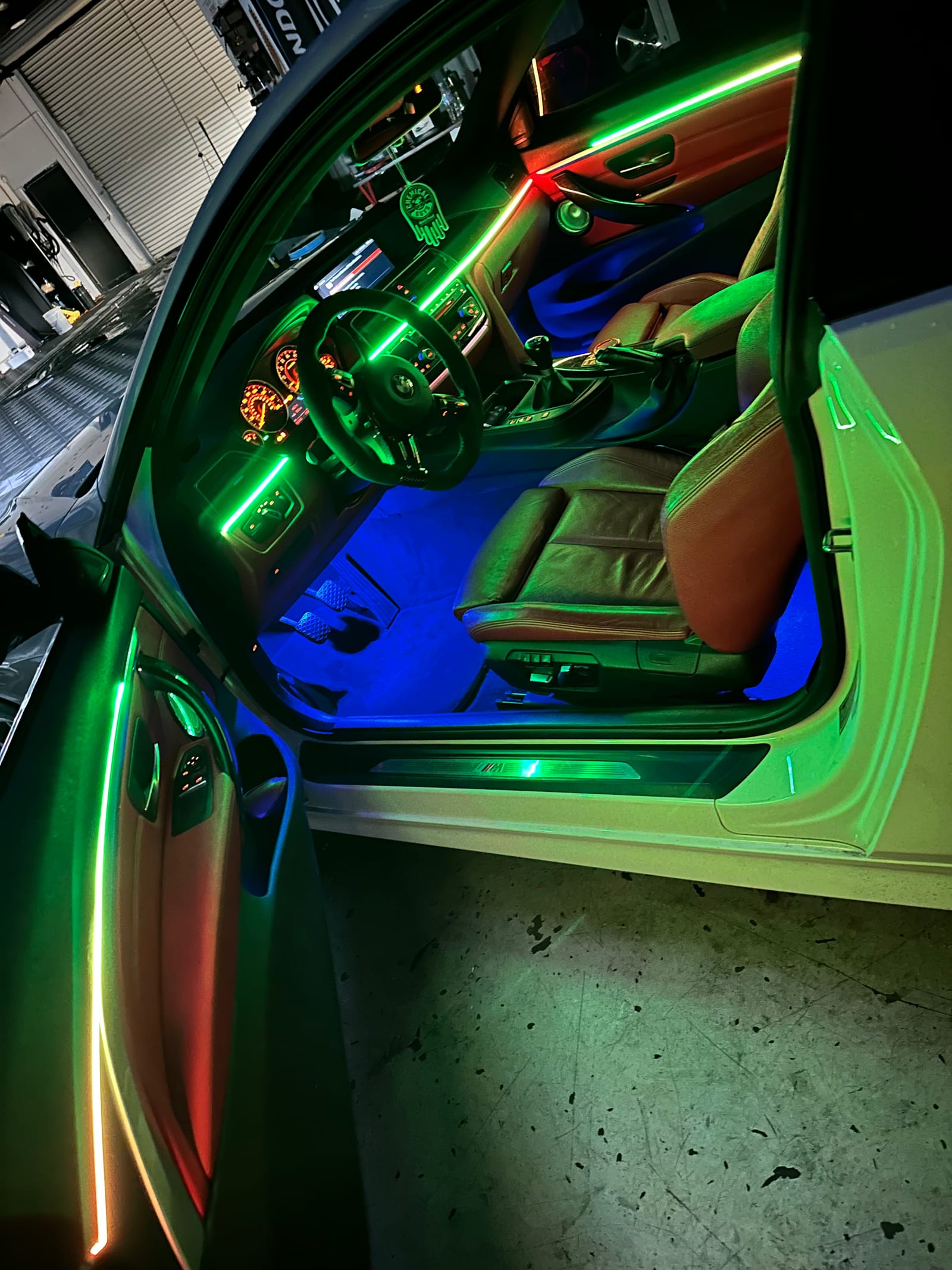 Green ambient light lines tracing the dash, doors, and steering wheel of a BMW with a blue footwell glow
