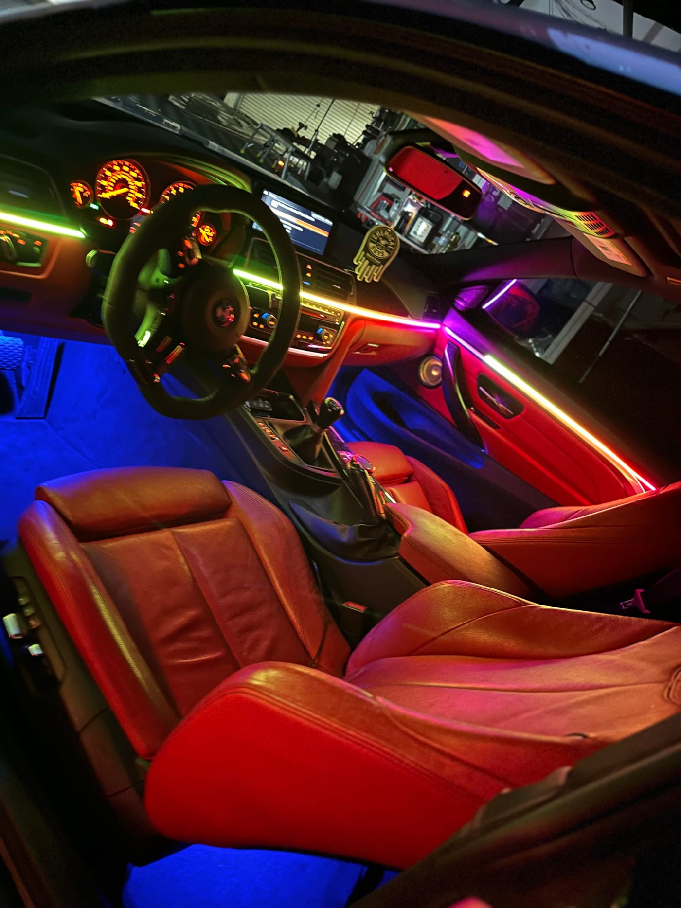 Rainbow gradient ambient light strip across the dash of a BMW with red leather interior