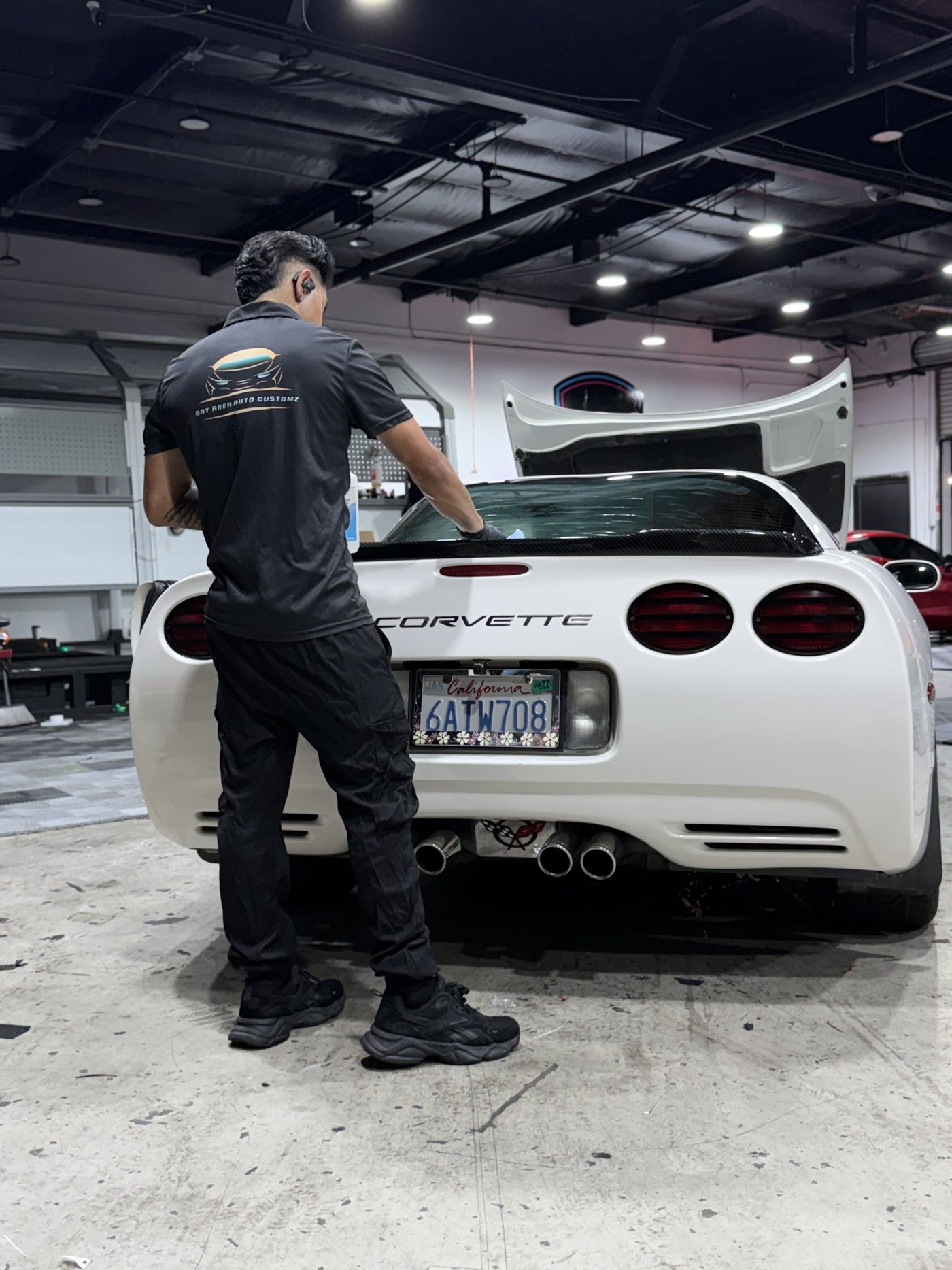 Sergio working across the rear deck of a white Corvette inside the Bay Area Auto Customz shop
