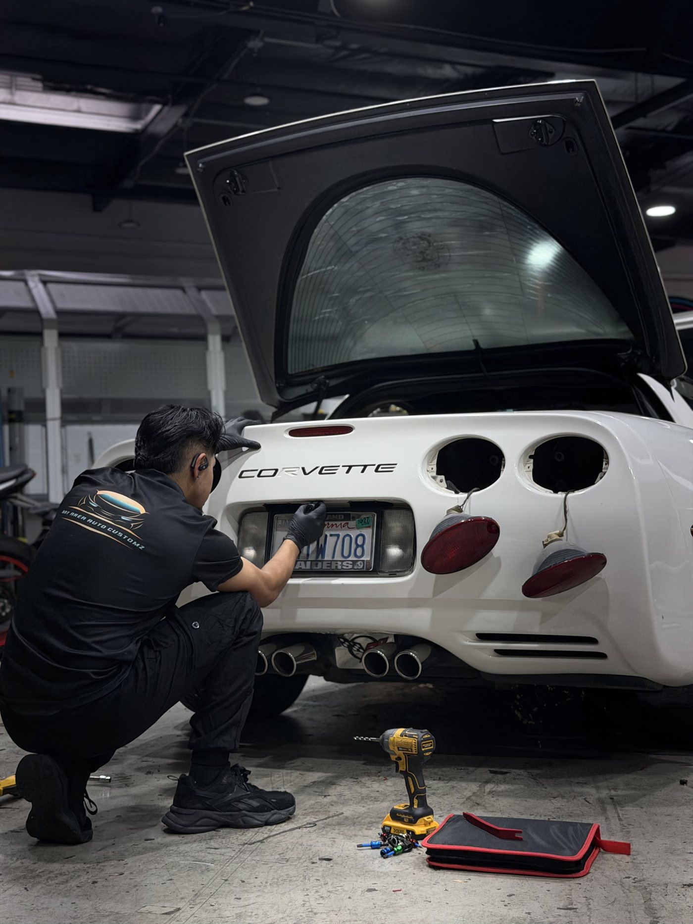 Installer crouched with tools during a careful rear teardown on the Corvette