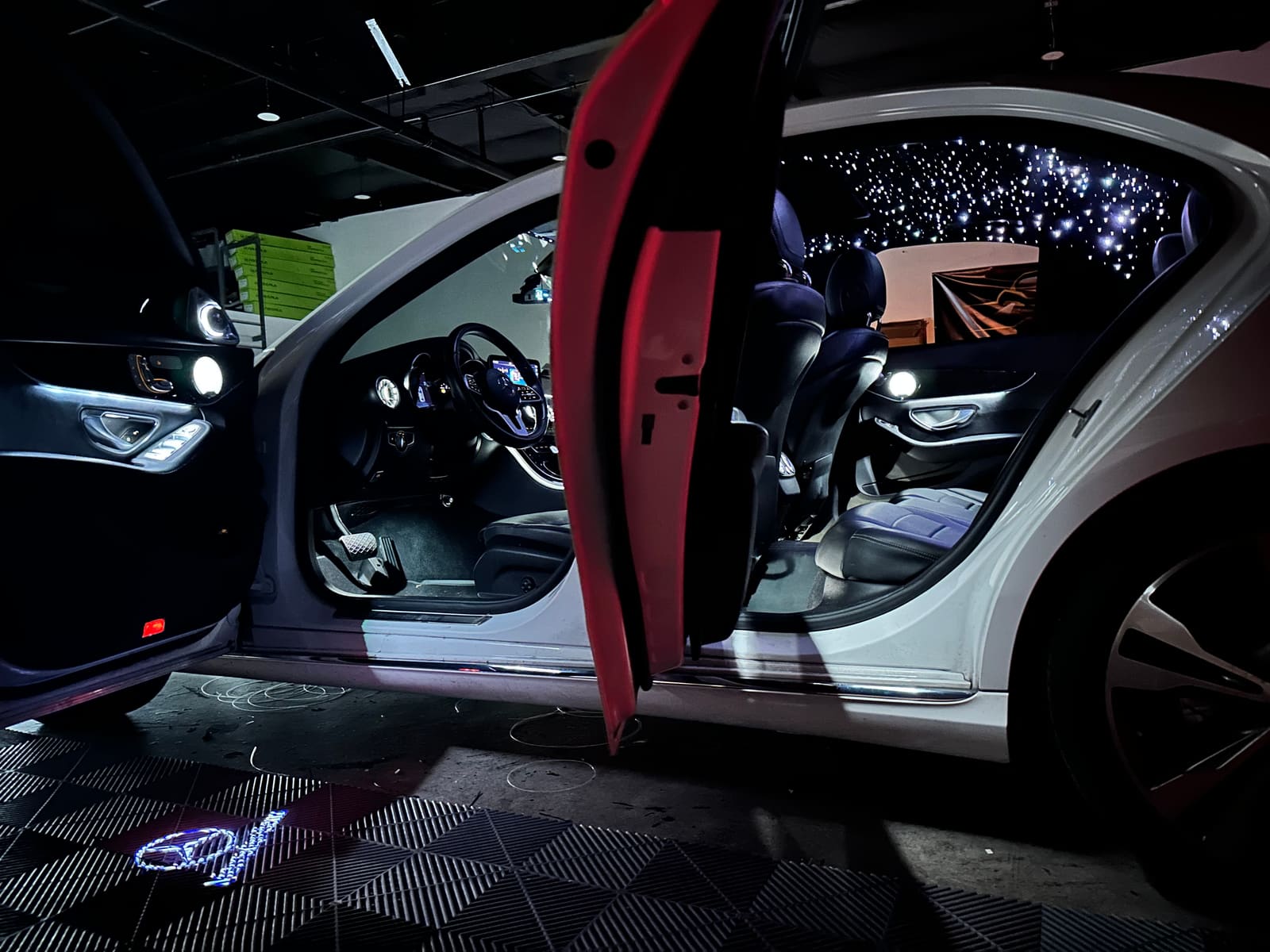 White Mercedes with doors open, starlight headliner lit and logo puddle lights on the shop floor